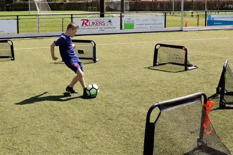 Jongen dribbelt met voetbal tussen kleine popup-doeltjes op kunstgras tijdens FIFA Skill Games