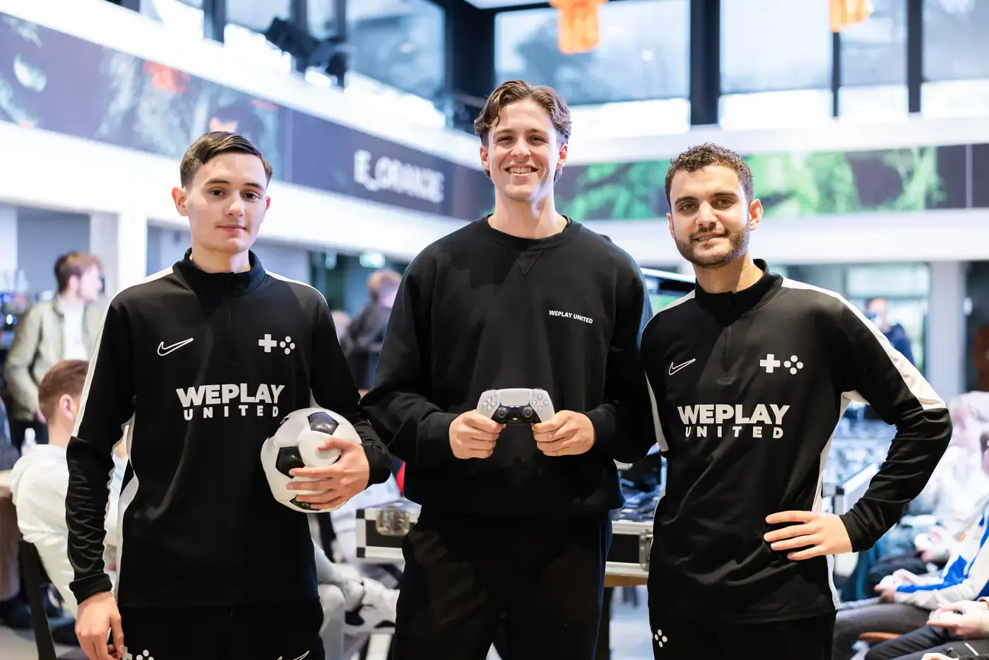 Drie WePlay United medewerkers poseren met een voetbal en PS5-controller op een FIFA-evenement