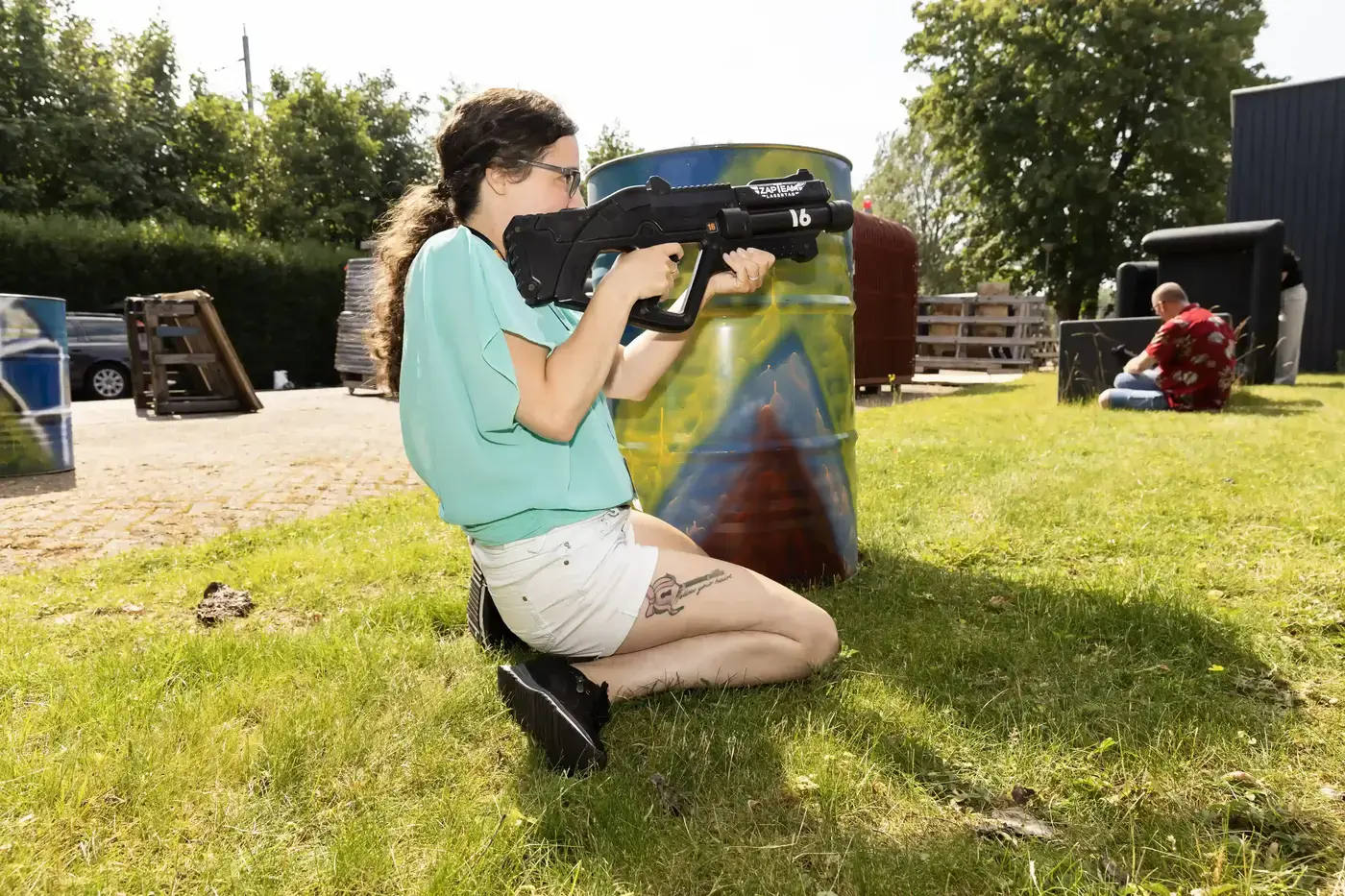 Vrouw knielt achter een beschilderd obstakel en richt haar laserwapen tijdens een buitenspel op het gras