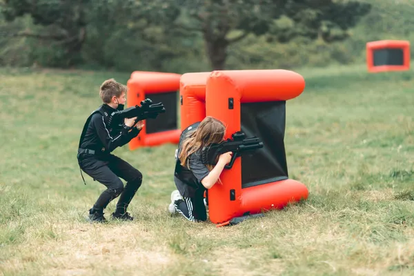 Jongen en meisje spelen lasergamen achter opblaasbare hindernissen op een grasveld