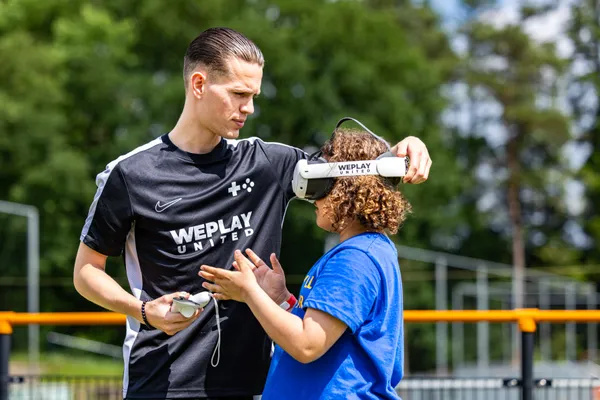 WePlay United medewerker helpt kind met VR-bril op een sportveld